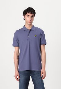 Violet polo marškinėliai su klasikine apykakle, trijų mygtukų užsegimu ir maža geltona siuvinėta logotipu ant krūtinės. Trumpomis rankovėmis.