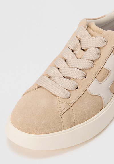 Baskets suédées beiges avec de grosses lacets crème, un détail latéral blanc et une semelle en caoutchouc blanche.