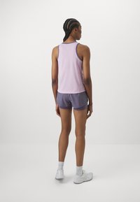 Heledat tooni lillad tank top, millel on tumelillad detailid, sobib tumelillade lühikesed püksid. Materjal näib olevat hingav, mõeldud aktiivseks kandmiseks. Näha on valged tossud.
