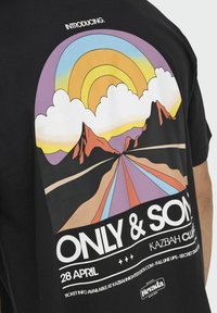 T-shirt in cotone nero con un design grafico colorato che presenta un arcobaleno, montagne e una strada. Il testo include "INTRODUZIONE" e i dettagli dell'evento.