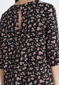 Musta kukkamekko, jossa on kolmannen neljänneksen hihat, avara selkäosa, herkät vaaleanpunaiset ja valkoiset kukkakuviot sekä teksturoitu kangas.