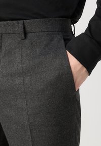 Grijze wollen broek met een gestructureerde afwerking, met een rechte pasvorm en zijzakken, gecombineerd met een zwart langarm T-shirt.