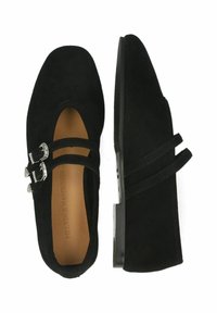 Sapatilhas de camurça pretas com bico redondo, apresentando duas fivelas ajustáveis em prata. Sola texturizada; design minimalista.