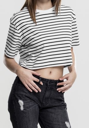 Witte crop top met zwarte strepen, gemaakt van zacht katoen, gecombineerd met zwarte high-waisted jeans met distressed details.