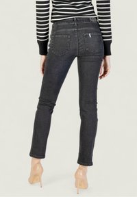Jeans de mezclilla gris oscuro con un diseño ajustado y bolsillos traseros, combinados con tacones altos nude. La tela tiene una textura suave.