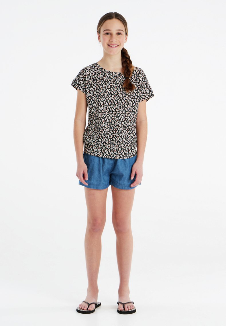 T-shirt nera a fiori con maniche corte, abbinata a pantaloni shorts in denim blu. L'outfit presenta una vestibilità comoda e uno stile informale.