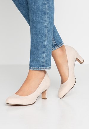 Beige suède hakken met een ronde neus en een lage blokhak. Ontworpen met een V-vormige opening en een gladde textuur, gedragen met blauwe denim jeans.