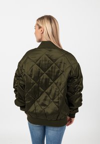 Giubbotto bomber imbottito verde oliva in tessuto satinato, con colletto a coste e polsini elasticizzati, caratterizzato da dettagli di cucitura a forma di diamante.