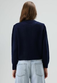 Marineblauwe cropped gebreide trui met een ronde halslijn en lange mouwen, met een gladde textuur en een geribbelde zoom, gecombineerd met lichtblauwe spijkerbroek.