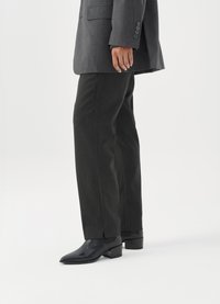 Ραμμένα παντελόνια γκρί κοστούμι σε λεπτό σχέδιο ψαροκόκαλο, σε συνδυασμό με γυαλιστερές μαύρες μποτες με μυτερή μύτη και φαρδύ τακούνι.