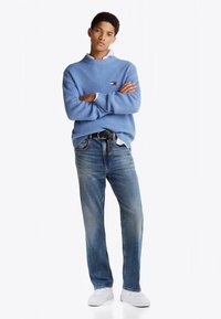 Svetlo modra rebrasta majica z visokim ovratnikom, nošena čez belo srajco, kombinirana s svetlo modrimi kavbojkami in belimi supergami. Enostaven dizajn in kroj.