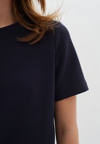 Tamsiai mėlyna medvilninė marškinėliai su trumpomis rankovėmis, apvalia iškirpte ir lygi tekstūra. Pasižymi minimaliai siūlėmis ir elegantišku, paprastu dizainu.