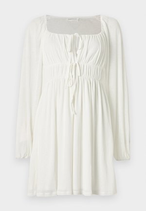 Robe mini blanche à manches longues avec encolure carrée, bustier et taille froncés, et deux liens à l'avant pour ajustement.