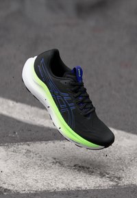 Black athletic shoe with a smooth design. Features blue accents, a textured upper, and a vibrant green sole for added contrast.