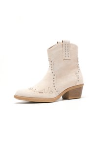 Botas de cowboy de ante en un tono beige claro, con costuras decorativas y tachuelas plateadas, un tacón corto y un diseño de punta afilada.