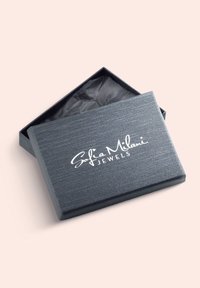 Scatola per gioielli nera con texture e una leggera lucentezza. Presenta un logo bianco in corsivo sul coperchio. Internamente foderata con carta velina nera.