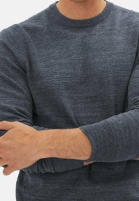 Pull en tricot gris foncé avec un col rond, des manches longues et des poignets côtelés, présentant une texture douce et un motif chiné subtil.