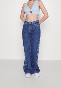 Hög midja, vida denimjeans i mörkblått med en subtil tryckt logotyp på vänster ben, tillsammans med en ljusblå kort topp.