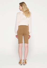 Maglione rosa chiaro a maniche lunghe abbinato a pantaloni corti marroni aderenti fino al ginocchio. Dettagli di cucitura visibili e una consistenza morbida in entrambi i capi.