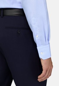 Lichtblauw geruit shirt met witte knopen, gedragen met marineblauwe broek, met een zachte textuur en een zakdetail op de broek.