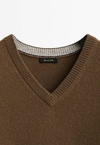 Pull en maille brun à col en V avec détail côtelé au col et encolure intérieure grise, avec une petite étiquette de marque noire à l'intérieur du col.