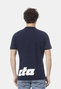 Polo navy blu in cotone, maniche corte, con testo del logo bianco sul retro, colletto classico e taglio dritto.