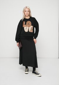 Černá mikina s velkým zlatým a bronzovým flitrovým nápisem "LOVE", doplněná dlouhou černou sukní a černými teniskami.