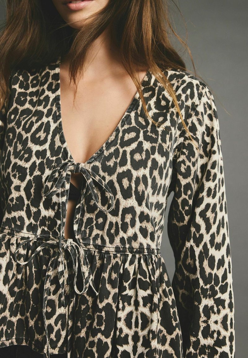 Leopardenmuster-Oberteil mit tiefem V-Ausschnitt, Bindeschluss und gerafftem Peplumsaum. Der Stoff hat eine weiche Textur in Schwarz und Creme.