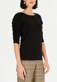 Czarna bluzka z bufkami, z marszczeniami, okrągłym dekoltem i wykonaną z gładkiego materiału, w zestawie z spodniami w kratę.