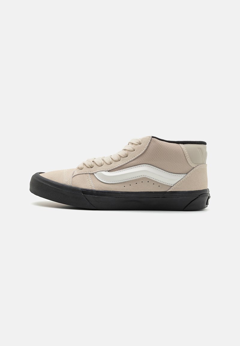 Høyt snøreskor med beige semsket skinn og mesh-overdel, hvit sidestripe og svart gummisåle. Runde snører og perforert detaljer.