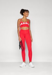 Conjunto atlético rojo que presenta un top corto con el logo "NEBBIA" y leggings de talle alto. El material parece suave, combinado con zapatillas blancas.