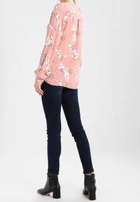 Rosa blommig blus med långa ärmar som har vita och gula blommor, kombinerad med mörka slim fit-jeans och svarta ankelstövlar. Slät tyg, avslappnad passform.