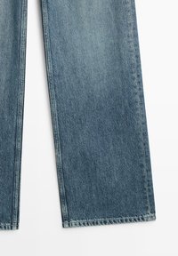 Recht gesneden blauwe spijkerbroekspijpen met subtiele vervaging en zichtbare stiksels op een witte achtergrond.