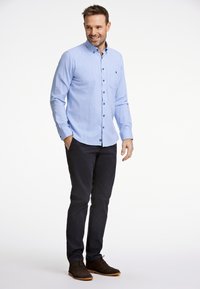 Ljusblå skjorta med knappar, bröstficka, långa ärmar, i kombination med mörkblå byxor och bruna stövlar. Slät textur, avslappnad passform.