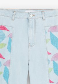 Jeans en denim bleu clair avec des motifs brodés colorés en rose, vert et bleu sur les côtés. Fermeture frontale standard avec un bouton.