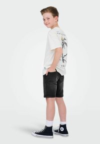 Vit t-shirt med palmträdsgrafik, matchad med svarta uppvikta shorts. Avslutar looken med blå höga sneakers och vita strumpor.
