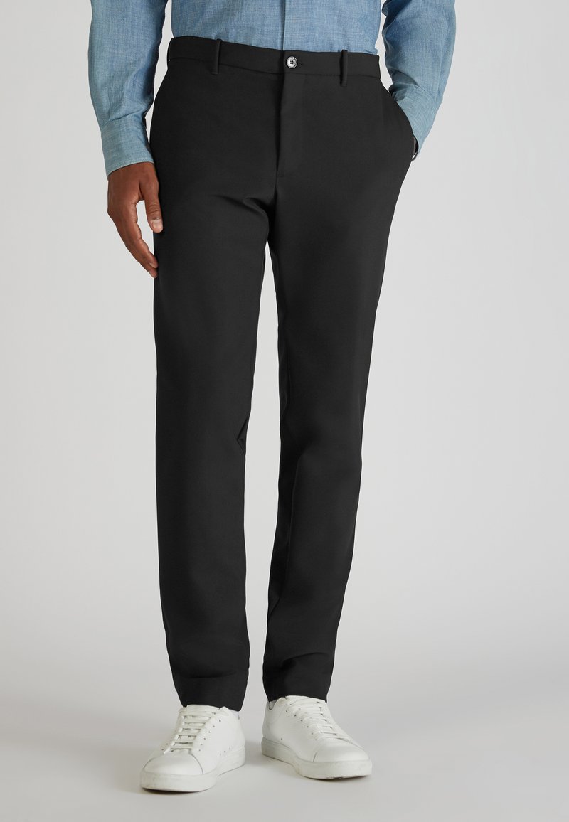 Zwarte broeken met een rechte pasvorm, voorzien van een knoopsluiting en riemlussen, gecombineerd met witte sneakers en een lichtblauw shirt.