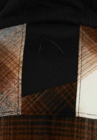 Combinación de tela de cuadros en marrón, crema y negro; presenta un panel negro contrastante con bordado; textura suave; diseño de patchwork.