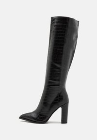 Bottes noires mi-mollet en similicuir brillant avec une texture crocodile, bout pointu et talon carré.