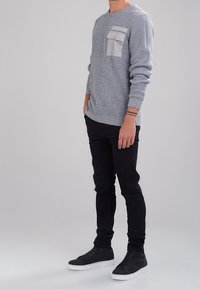 Grå texturerad tröja med en framficka, kombinerad med svarta slim fit-byxor och mörka sneakers. Uttrycket har en avslappnad design.