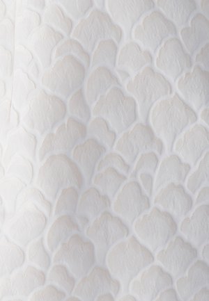 Texturovaná látka v jemně bílé barvě s vyvýšenými, scalloped vzory. Materiál se zdá být měkký s jemným leskem a reliéfními detaily.