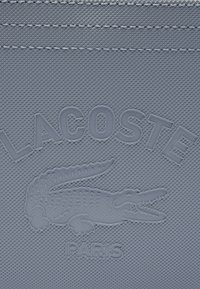 Tessuto strutturato blu chiaro con un logo in rilievo a forma di coccodrillo e il testo "LACOSTE" sopra e "PARIGI" sotto.