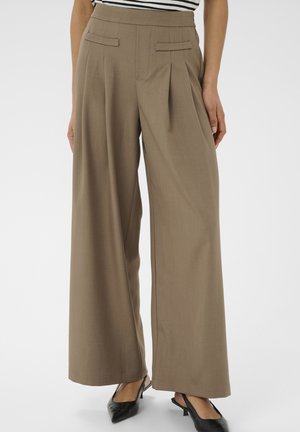 Beige Hosen mit weitem Bein, mit Falten und verdeckten Vordertaschen, kombiniert mit schwarzen Slingback-Schuhen mit niedrigem Absatz und einem gestreiften Oberteil.