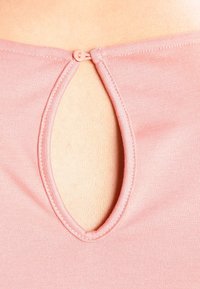 Różowy materiałowy top z okrągłym wycięciem na plecach, wykończony małym zapięciem na guzik. Gładka tekstura i luźny krój.