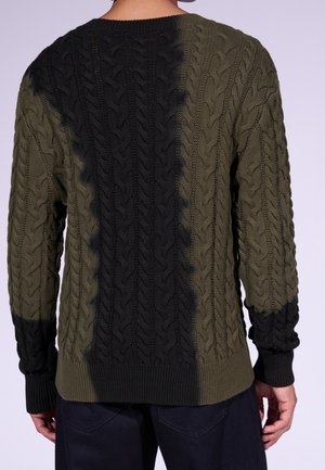 Osoba nosící zelený a černý svetr pletený copánkovým vzorem s černým svislým pruhem uprostřed a černými žebrovanými manžetami, zobrazená zezadu.