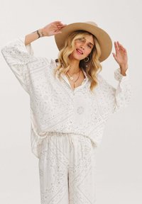 Bílý top s paisley vzorem, volného střihu, s výstřihem do V a dlouhými rukávy; kombinovaný s kalhotami na elastický pas ve stejném provedení. Hnědý plstěný klobouk.