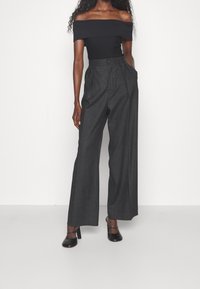 Top nero a spalle scoperte in maglina abbinato a pantaloni grigi a gamba larga e alta vita. L'outfit presenta dettagli minimali e linee di design moderne.