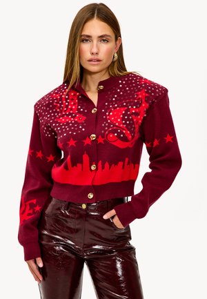 Cardigan bourgogne avec des motifs graphiques rouges, des boutons dorés et des sequins. Présente un ourlet court et un pantalon noir brillant uni.