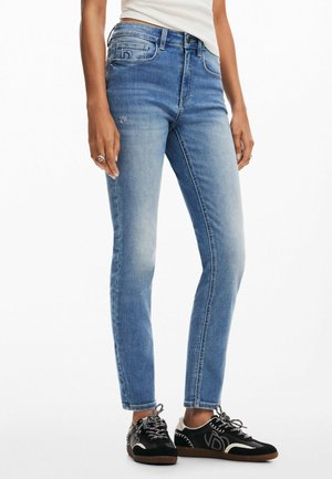 Jean bleu skinny avec une finition décolorée et un design à cinq poches. Portés avec des baskets noires présentant des accents blancs et des lacets texturés.