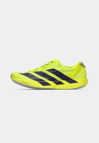 Φωτεινό κίτρινο αθλητικό παπούτσι με μαύρες ρίγες. Ελαφρύ σχέδιο, στρογγυλεμένη μύτη και ελάχιστο τακούνι. Υφή υφάσματος και λεπτομέρειες με επενδεδυμένο γιακά.